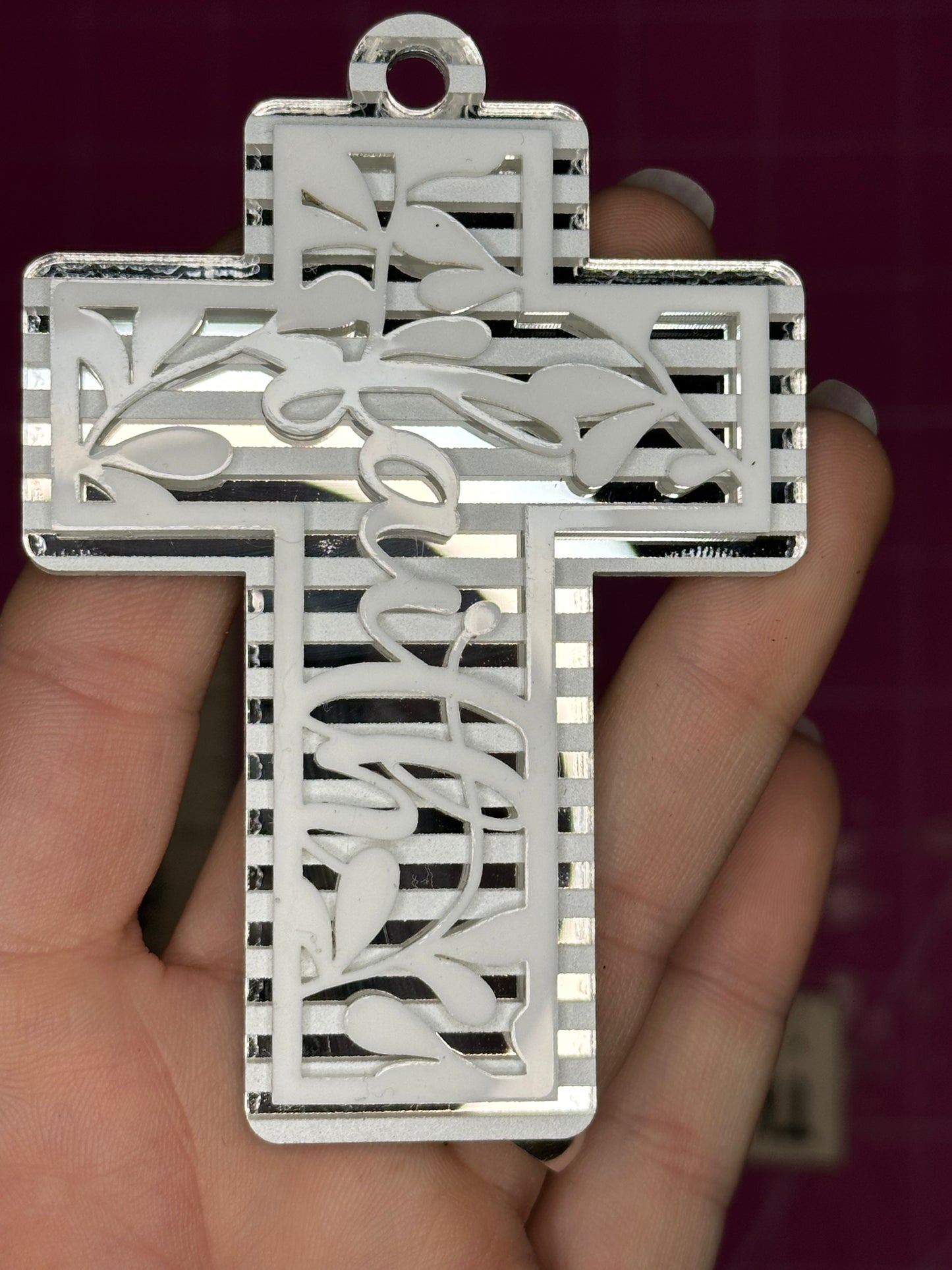 Silver cross pendant with intricate designs held in a hand against a dark background
