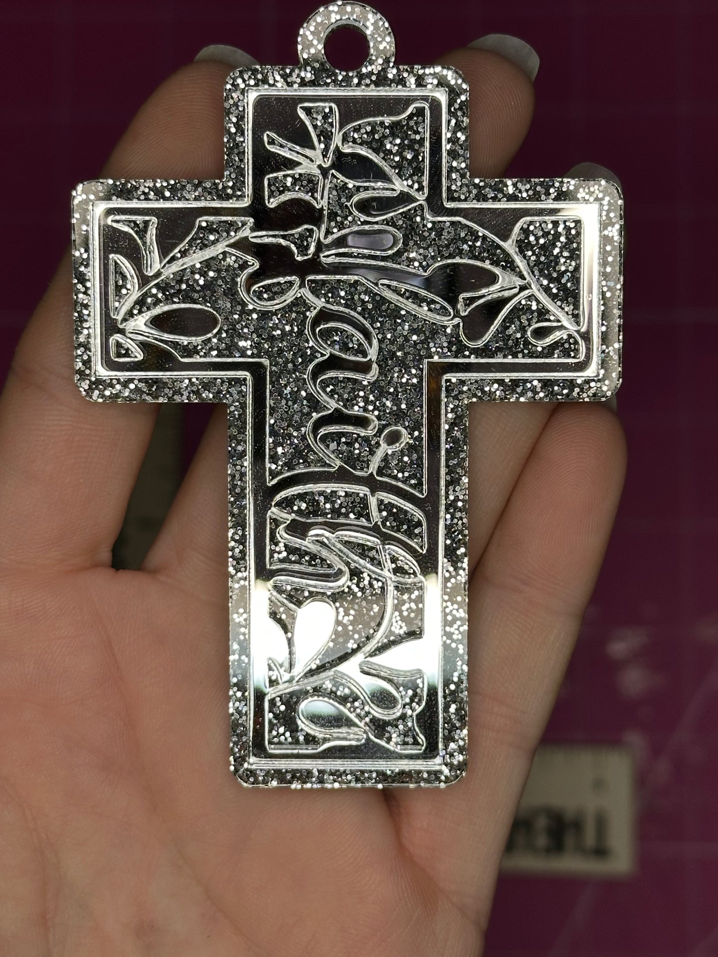 Silver cross pendant with intricate designs held in a hand against a dark background